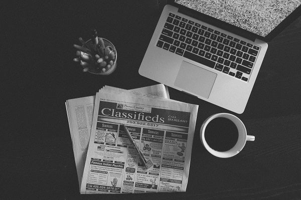A laptop, a cup of coffee, and a classifies newspaper